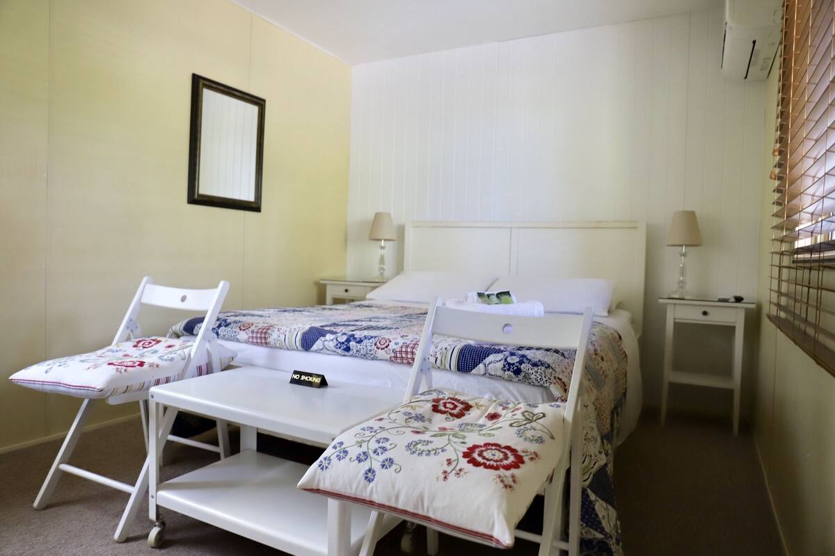 Ein Schlafzimmer mit einem Bett, zwei Nachttischen, einem Sessel, einem kleinen Tisch und einer Wandlampe.