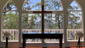 Una habitación con un piano de madera, amplias ventanas en arco y una cruz en el centro.
