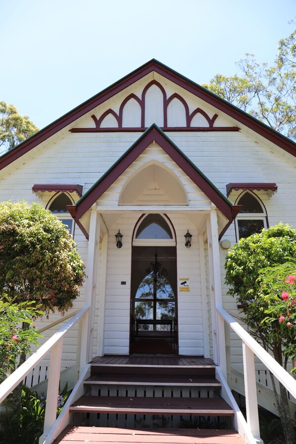 A white building with a brown roof, a front door, and a staircase leading up to the entrance. - Hilltop on Tamborine (Wongawallan)
