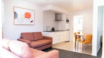 Una sala de estar moderna con un sofá, un comedor con sillas, una cocina con estufa y microondas, y un cuadro en la pared.