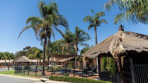 Un resort con cabañas de techo de paja, palmeras y un estacionamiento cercado.