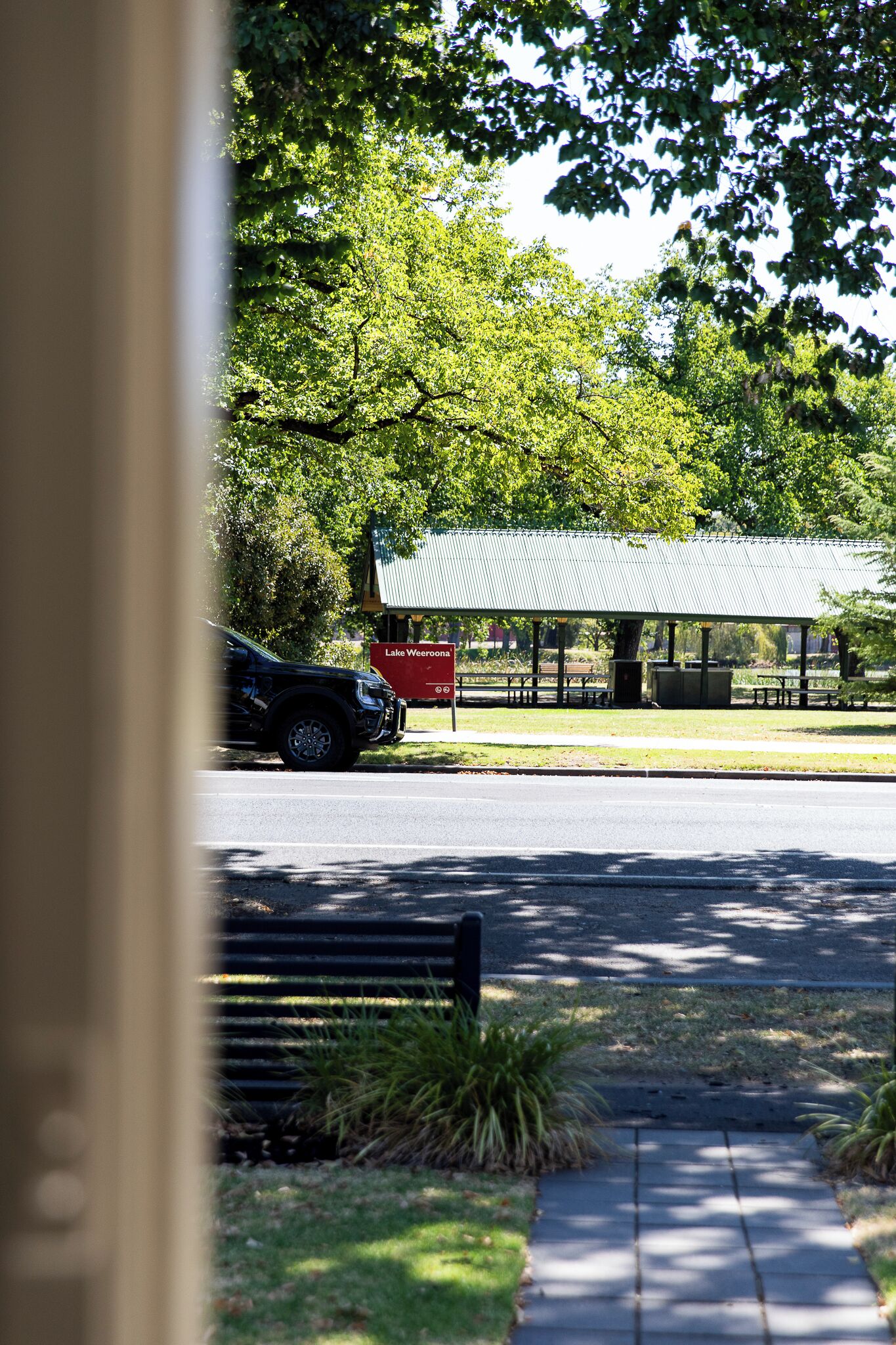A park with a covered pavilion, benches, and a car parked nearby.