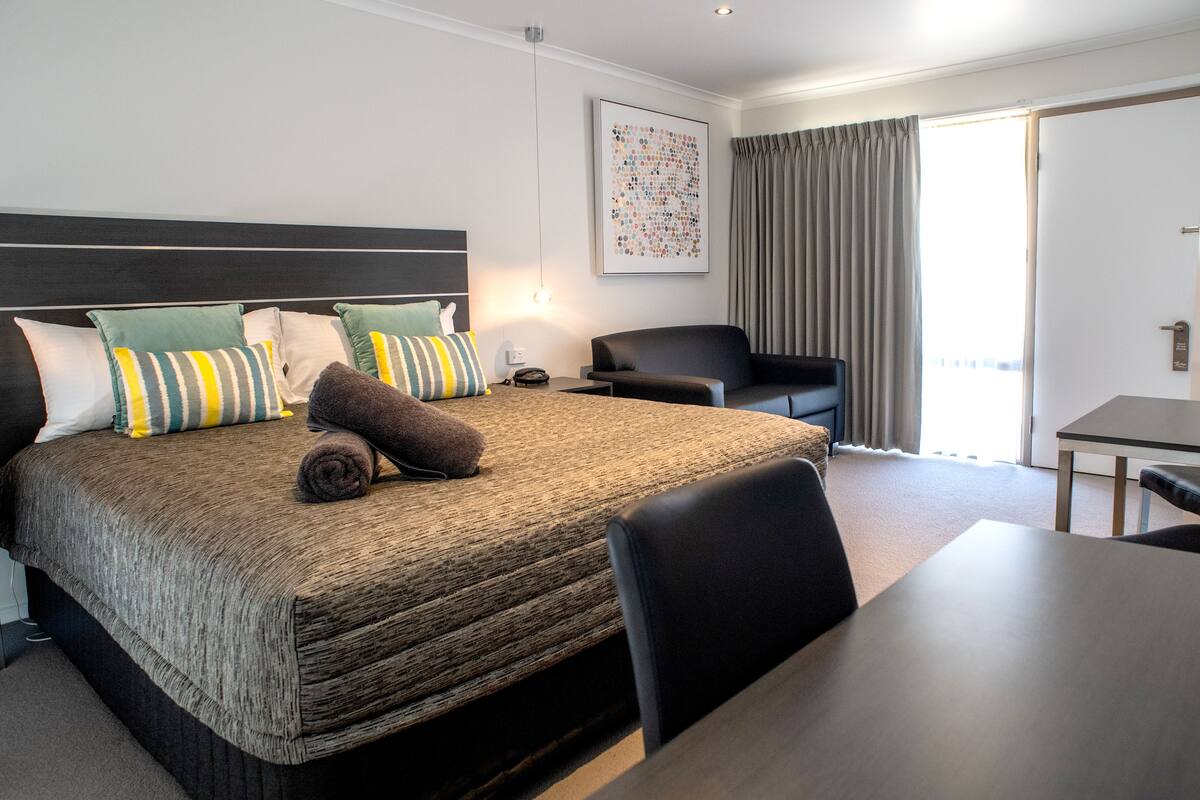 A hotel room with a large bed, a desk, a chair, and a view of the outdoors.