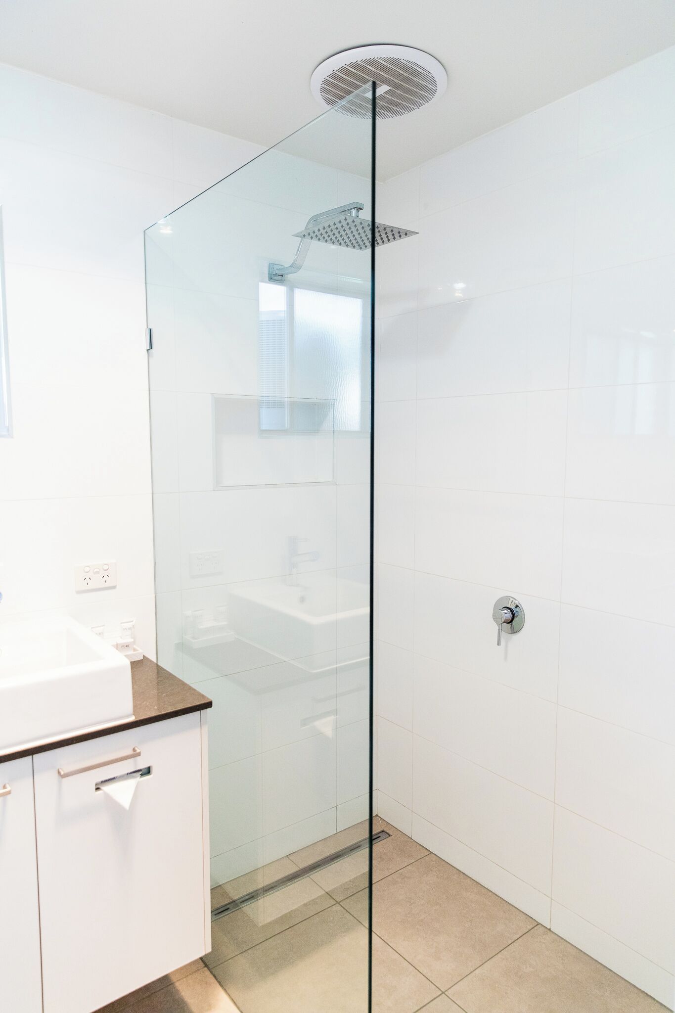 Un baño moderno con ducha envuelta en vidrio, azulejos blancos y una zona de lavabo visible.