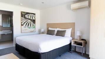 Une chambre d’hôtel moderne avec un grand lit, des tables de chevet avec des lampes, une salle de bain avec un lavabo et un tableau au mur.