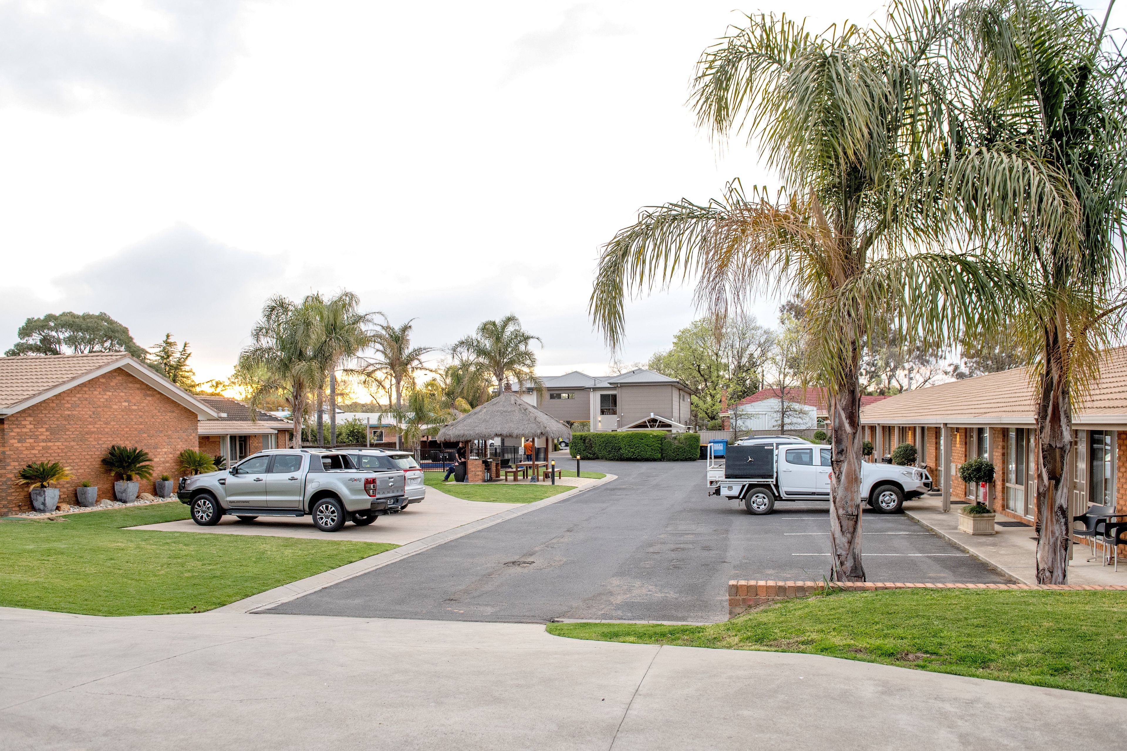 A residential street with parked cars, houses, and a small gazebo.