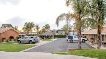 A residential street with parked cars, houses, and a small gazebo.