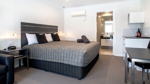 Una habitación de hotel moderna con una cama grande, una mesita de noche y un escritorio pequeño. Cuenta con un rincón de cocina equipado con microondas y lavamanos.