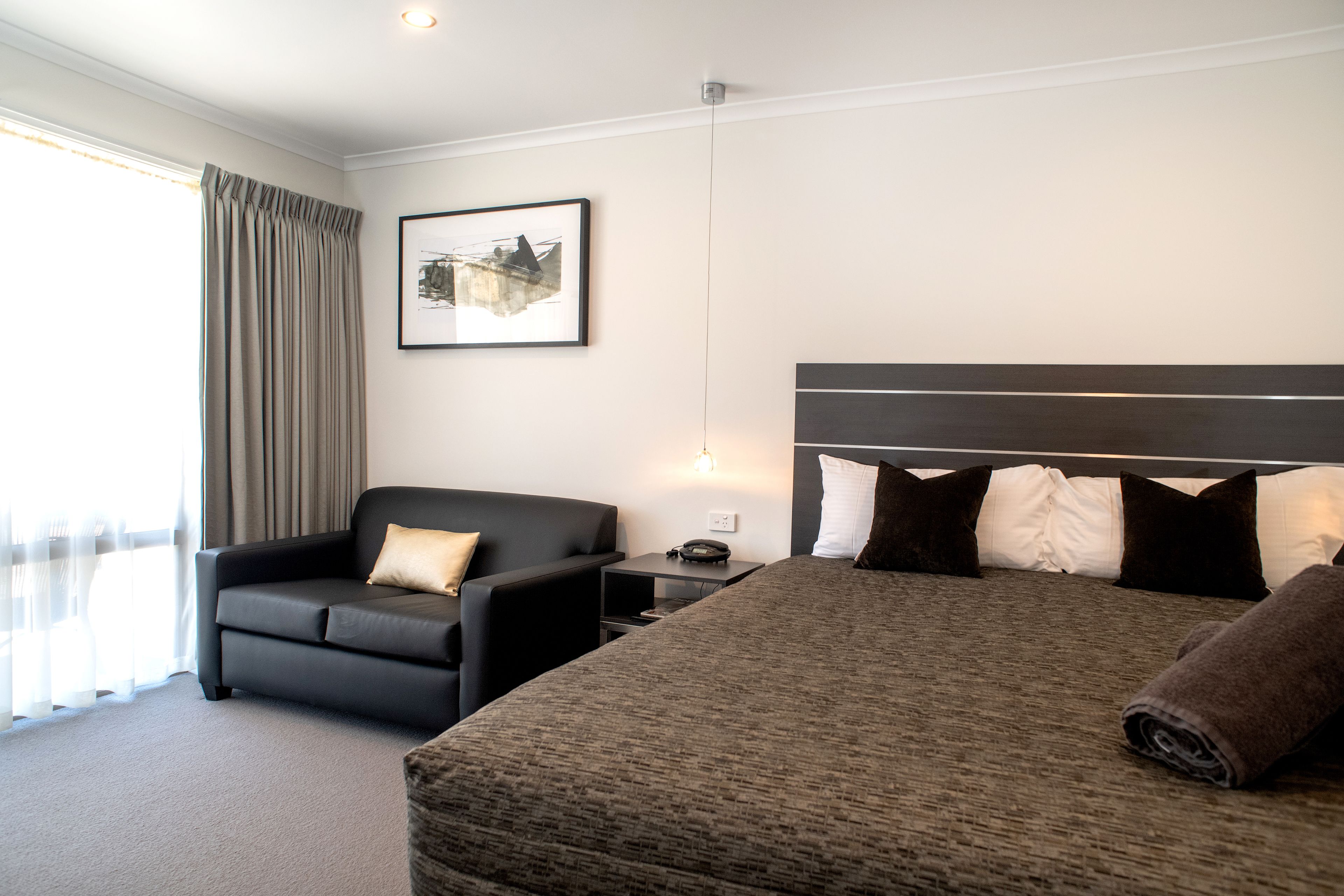 Habitación de hotel con una cama grande, un sofá, una mesita de noche y un cuadro en la pared.