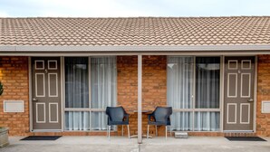 A building with a tiled roof, two doors labeled 5 and 6, and two black chairs in front of a window with curtains.