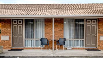 Un edificio con tejado de tejas, dos puertas con las etiquetas 5 y 6, y dos sillas negras frente a una ventana con cortinas.