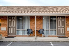 A building with a tiled roof, two doors labeled 5 and 6, and two black chairs in front of a window with curtains.