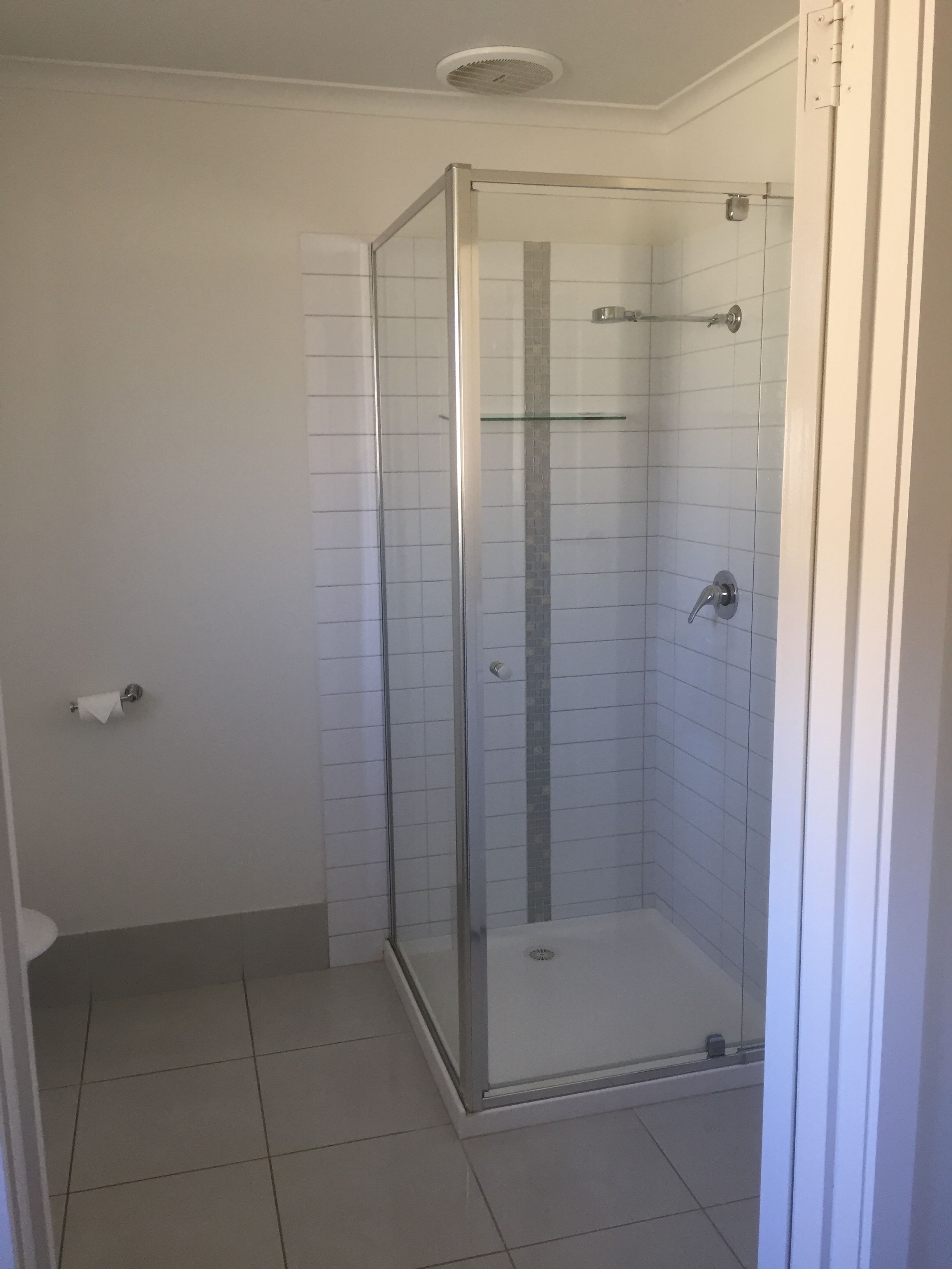 A glass-enclosed shower with a tiled floor and a wall-mounted towel holder.