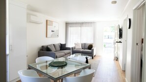 Una sala de estar moderna con dos sofás grises, una mesa de comedor de vidrio y sillas blancas.