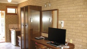 Une pièce compacte comprenant un coin cuisine, un bureau en bois avec un ordinateur, une chaise et un grand miroir.