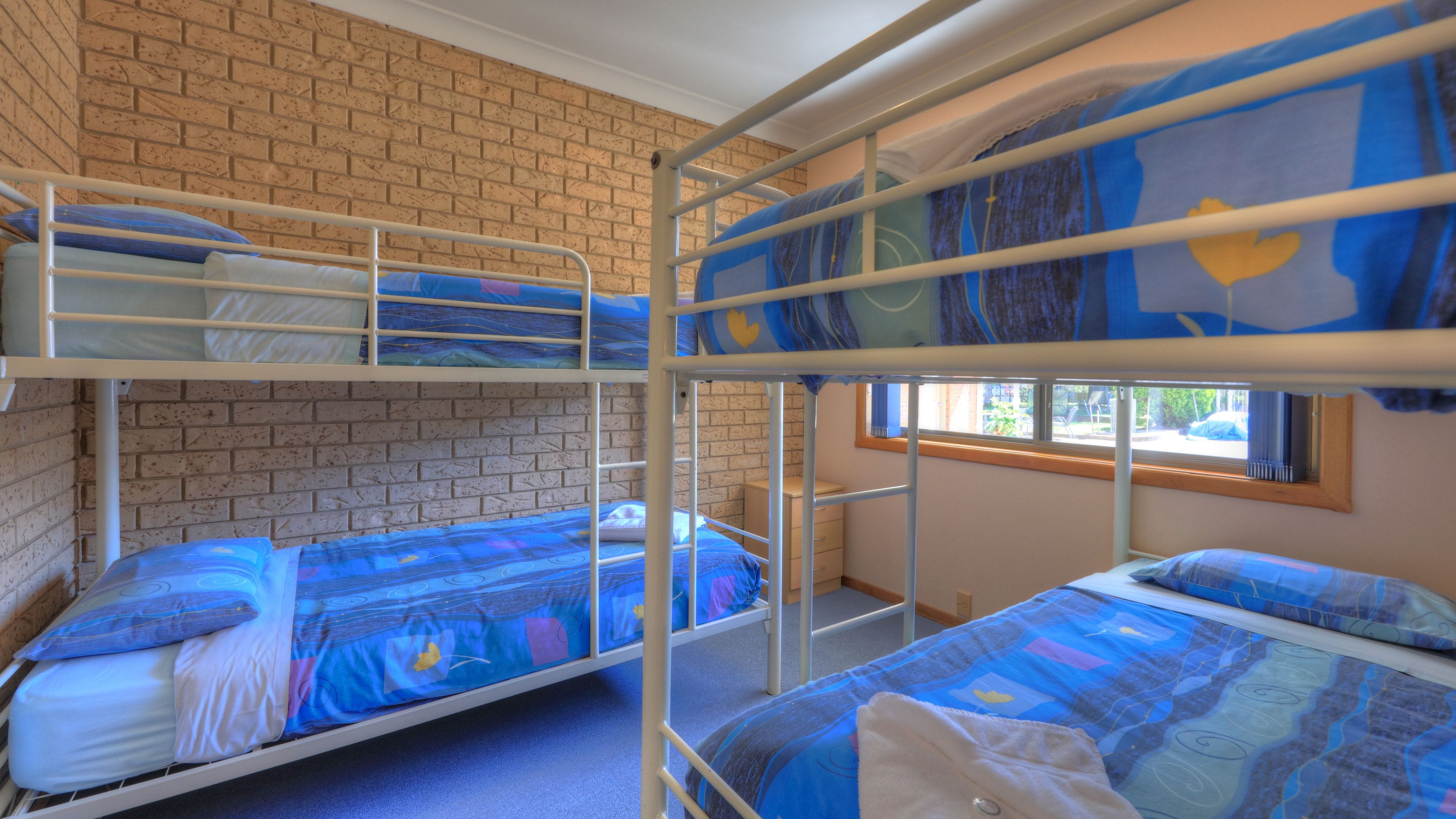 Quarto com beliche, parede de tijolos e janela.