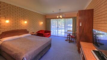 A hotel room with a bed, a red chair, a table with chairs, and a wooden cabinet.