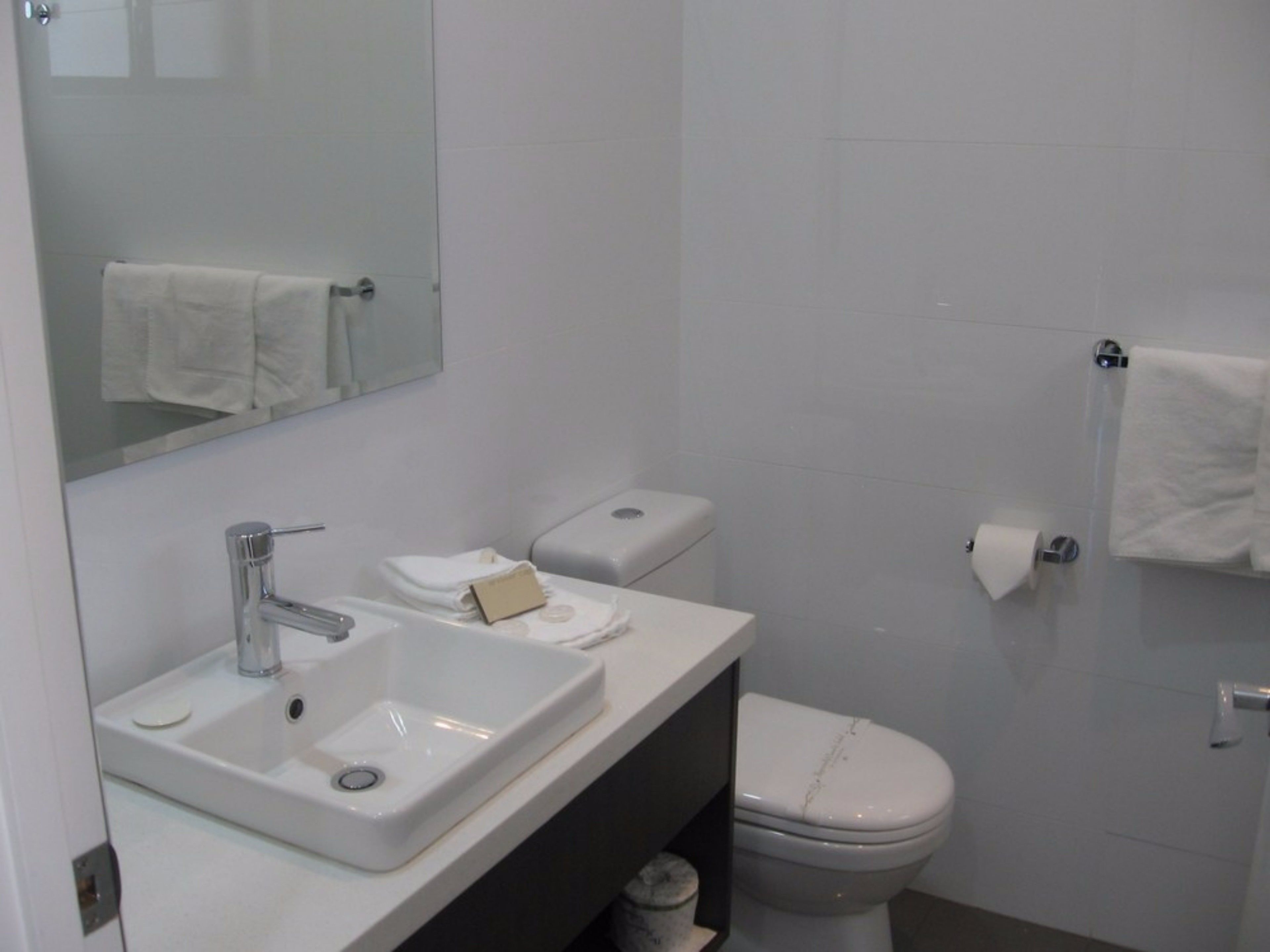 A modern bathroom with a white sink, mirror, and toilet.