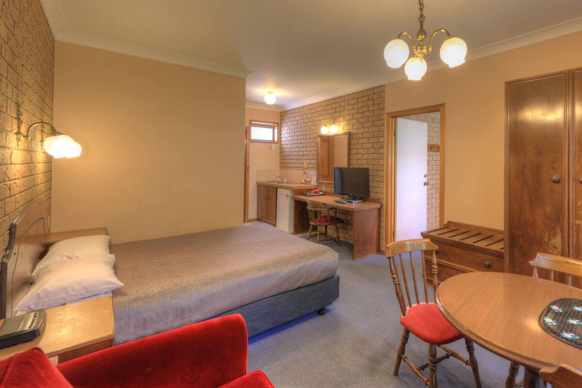 A bedroom with a bed, a desk, a chair, a table, and a television.