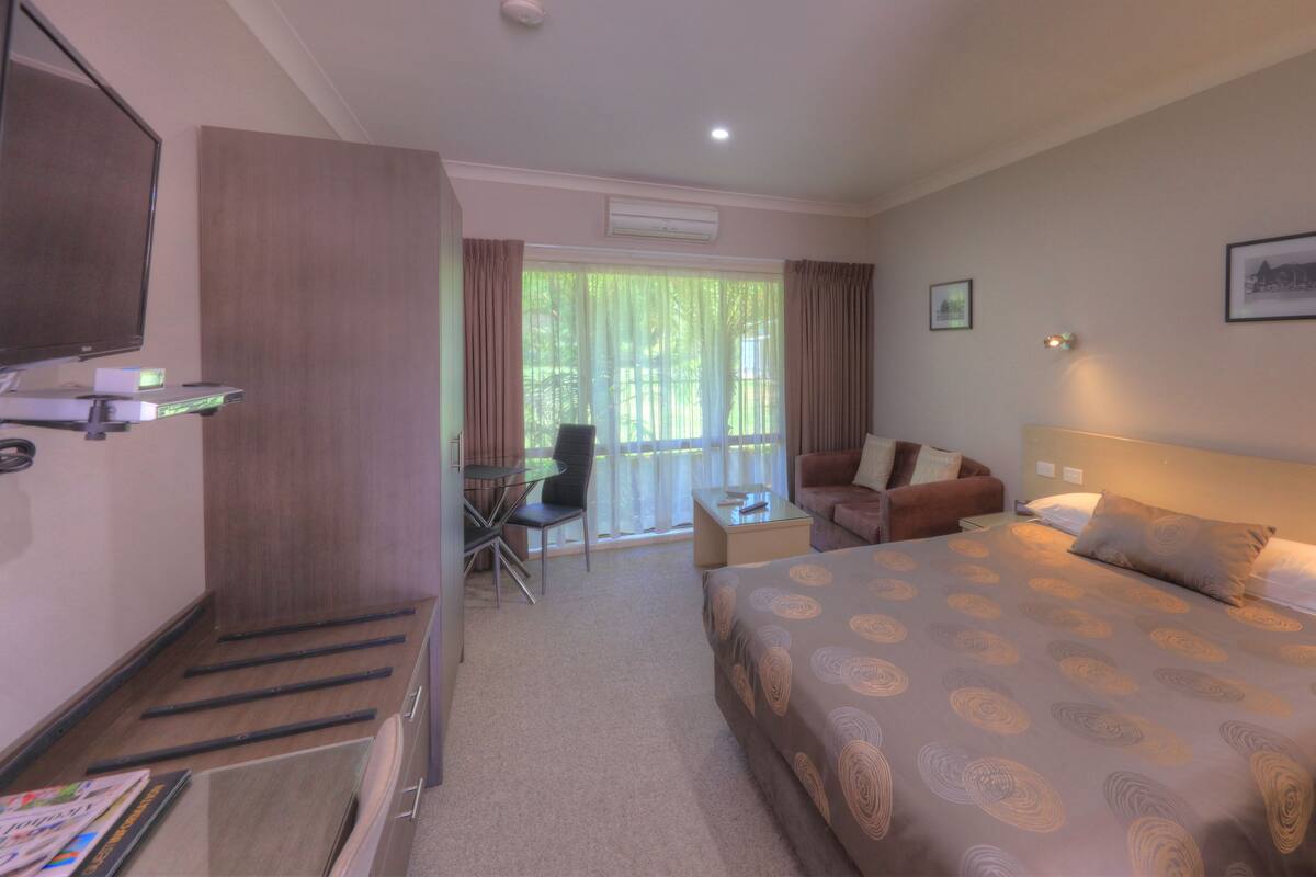 A hotel room with a large bed, a desk, a chair, a television, and a balcony with curtains.