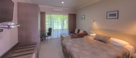 A hotel room with a large bed, a desk, a chair, a television, and a balcony with curtains.