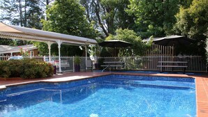 Une piscine dotée d’une terrasse carrelée, entourée d’une clôture et d’arbres.