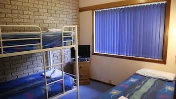 Une chambre de dortoir avec des lits superposés, un téléviseur, une fenêtre avec des stores et une commode.