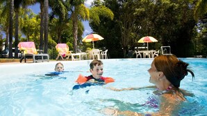 A swimming pool with lounge chairs and umbrellas, surrounded by trees. - Acclaim Kingsway Tourist Park (Madeley)