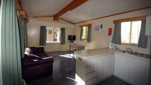 A compact living space with a sofa, a small dining table, a kitchenette, and a TV. - Acclaim Kingsway Tourist Park (Madeley)