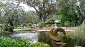 Un parque tranquilo con un estanque, abundante vegetación y una escultura peculiar.