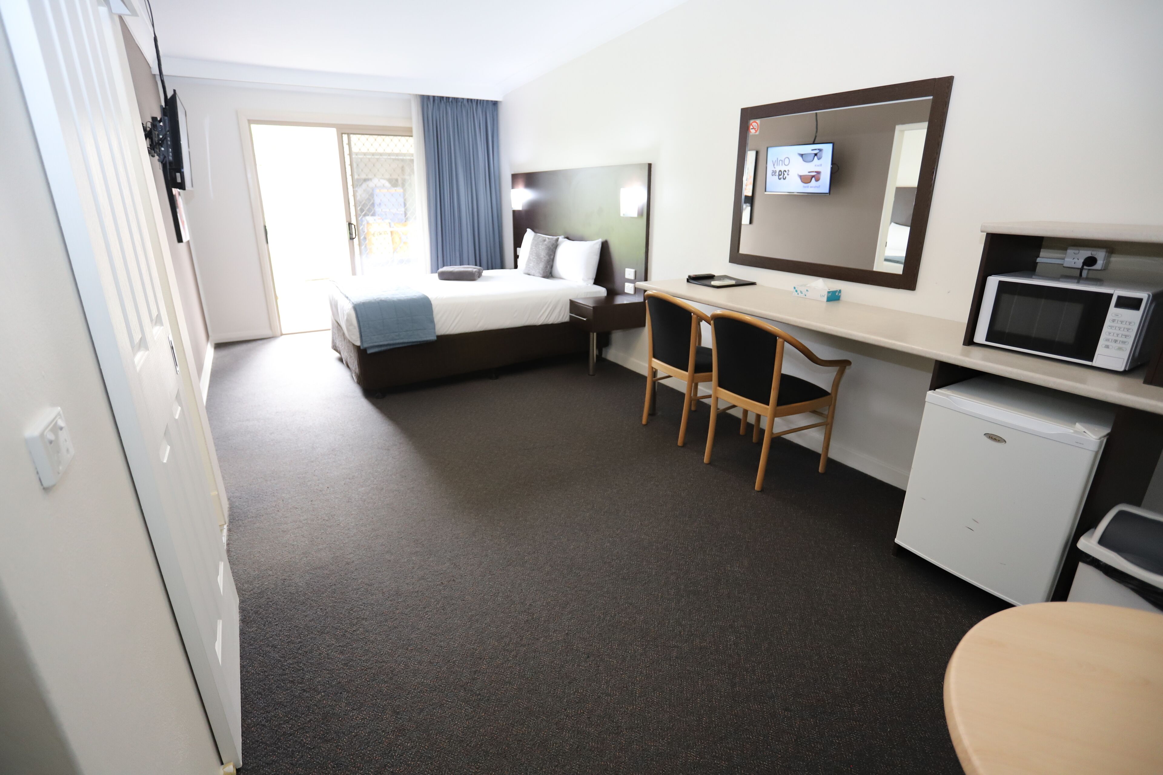 Een hotelkamer met een bed, bureau, stoel, magnetron en een kleine koelkast.
