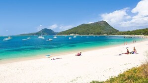 Una playa con agua turquesa cristalina, barcos y una montaña al fondo.