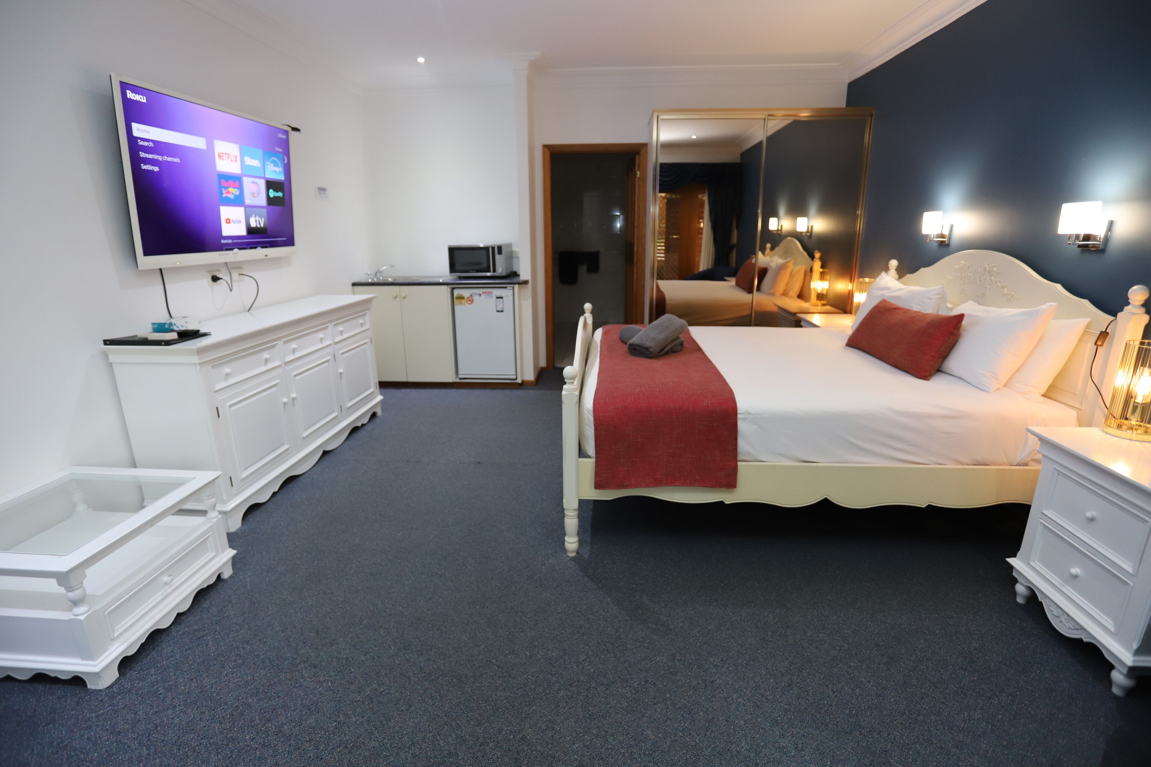 A hotel room with a bed, a TV mounted on the wall, a dresser, and a microwave.