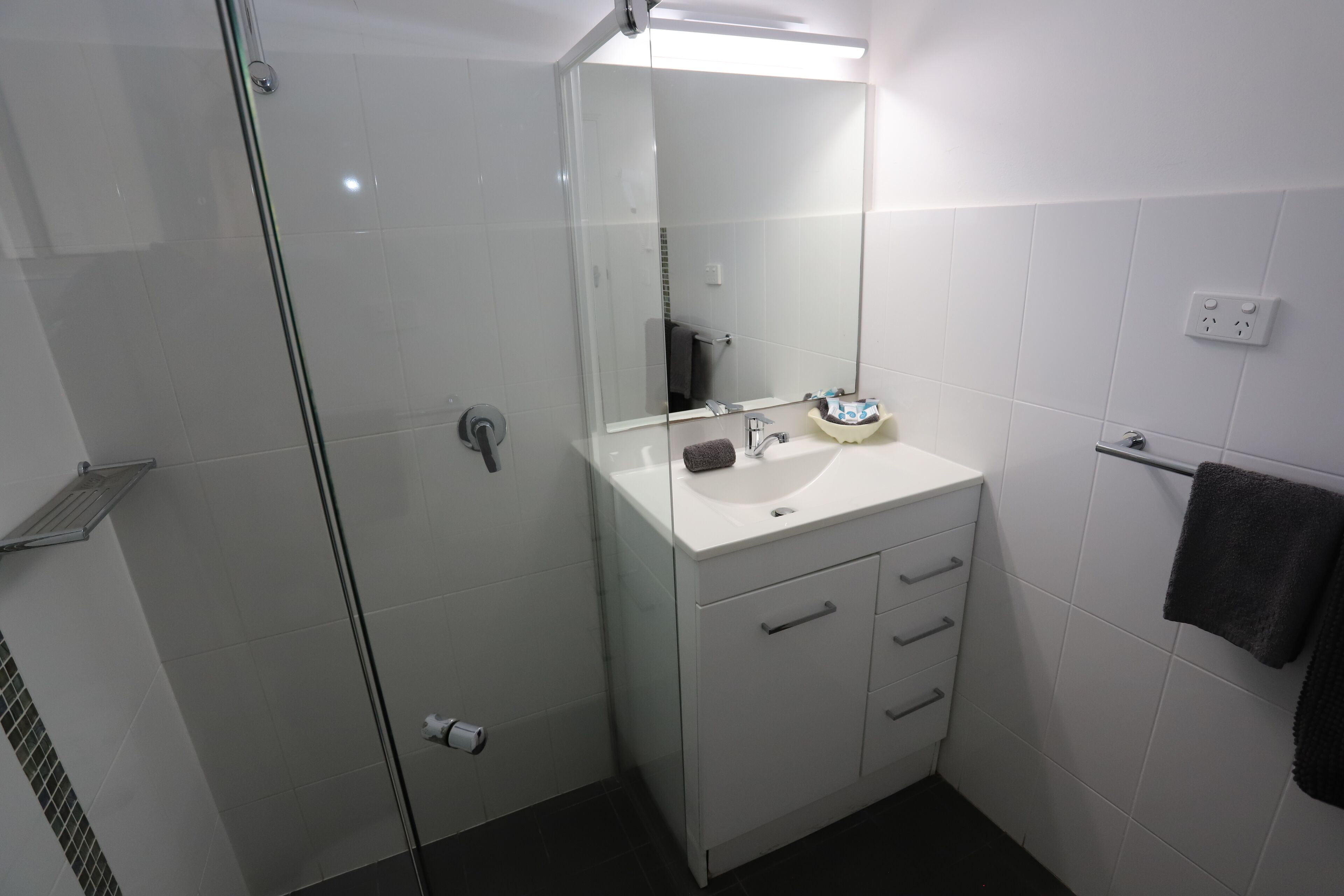 A modern bathroom with a glass shower enclosure, a white sink with a mirror above it, and a towel rack on the wall.