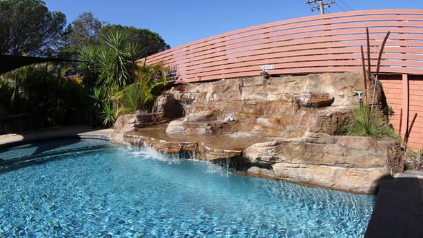Una piscina cristalina con una cascada rocosa y una estructura de techo curva roja.