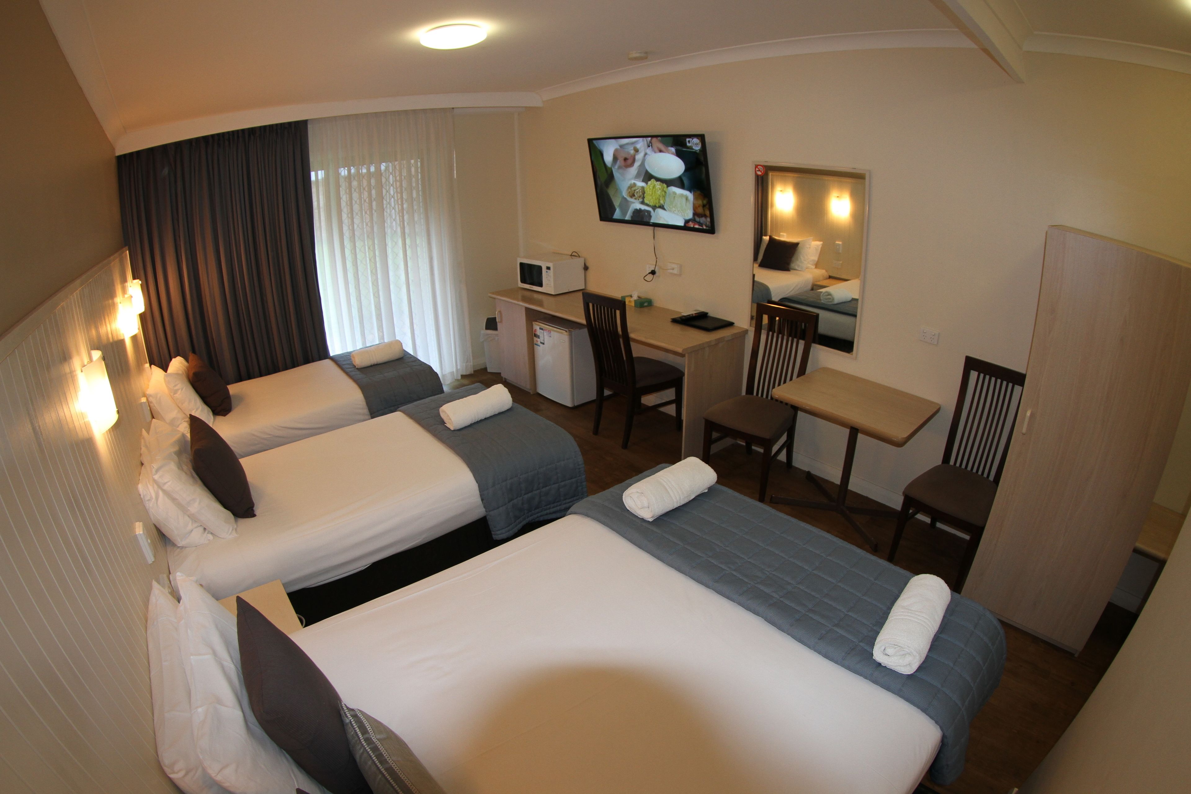 A hotel room with two beds, a desk, a chair, a TV, and a microwave.