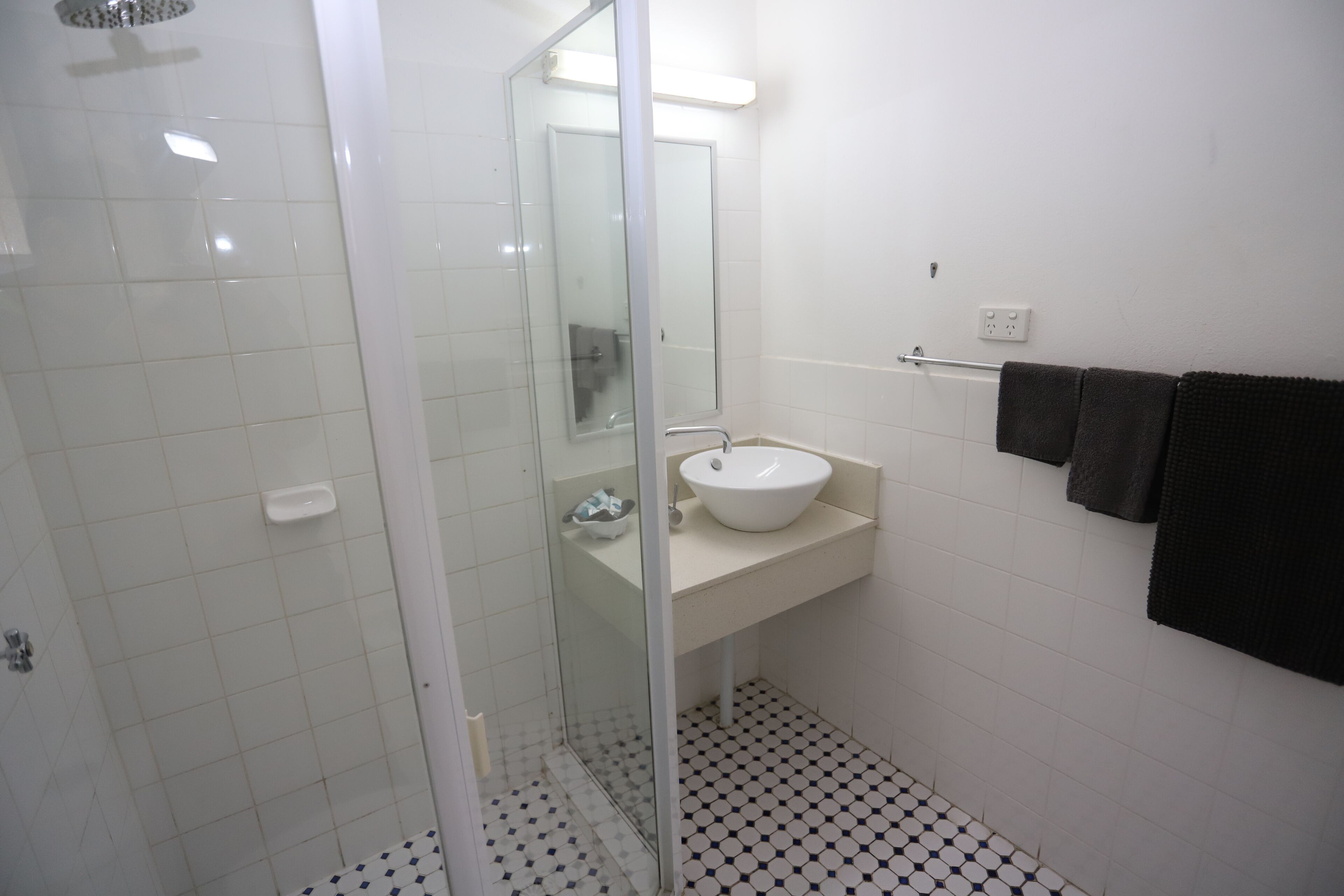 A bathroom with a glass-enclosed shower, a white sink, and a tiled floor.