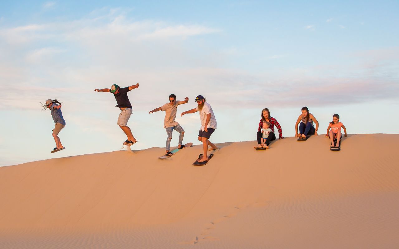A group of people on a sandy slope with a clear sky in the background.
