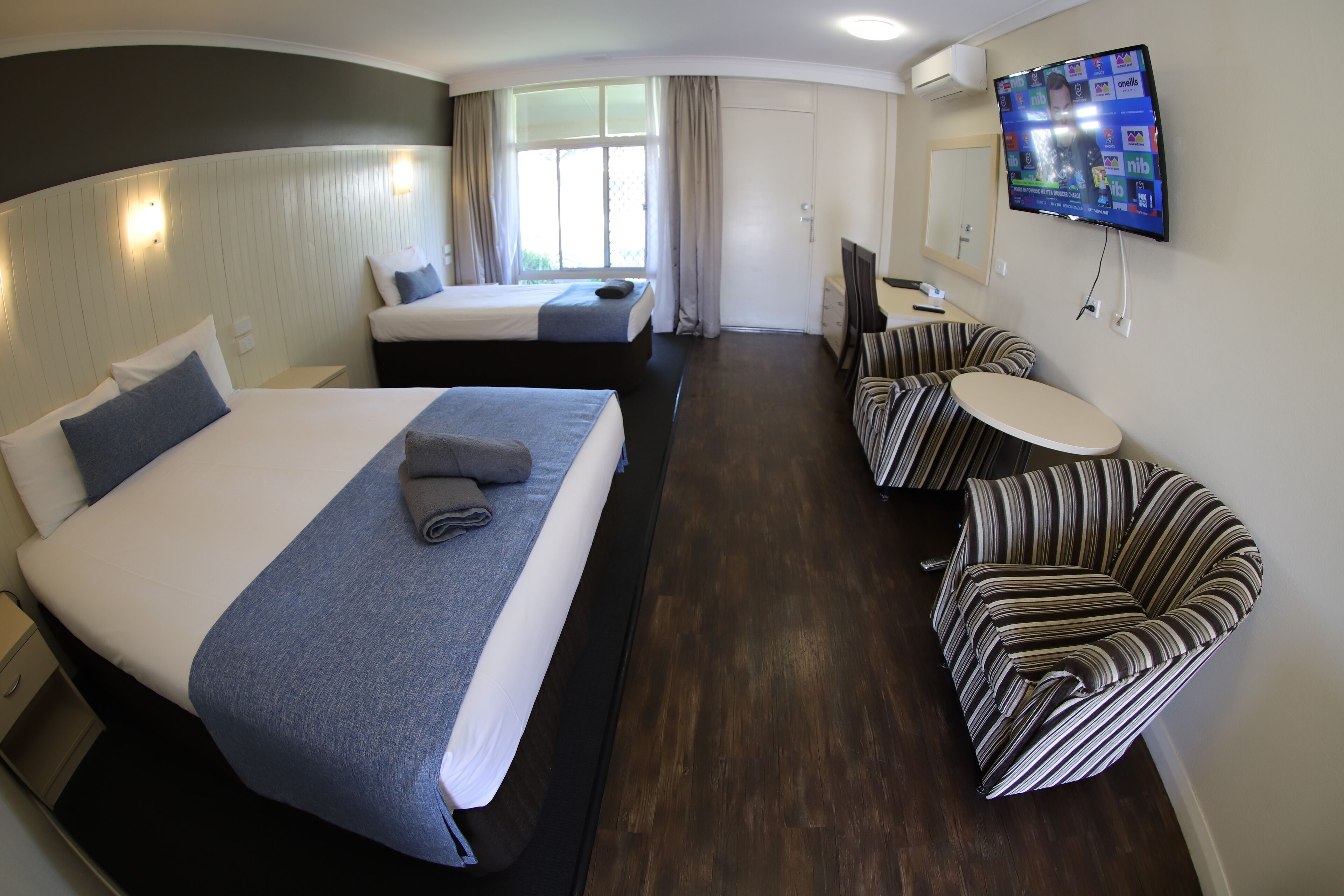 A hotel room with two beds, a TV, a small table, and a striped chair.