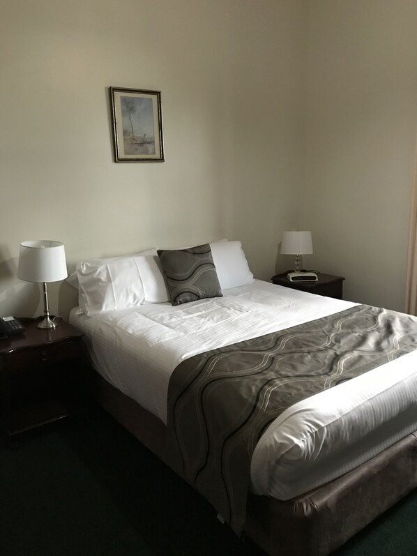 A neatly made bed with a patterned bedspread, two bedside lamps, and a framed picture on the wall.