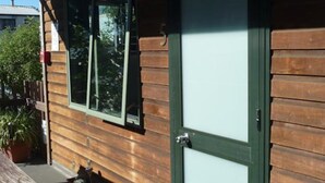 Une façade en bois, une porte coulissante en verre et un petit espace extérieur aménagé avec un banc et des plantes en pot.