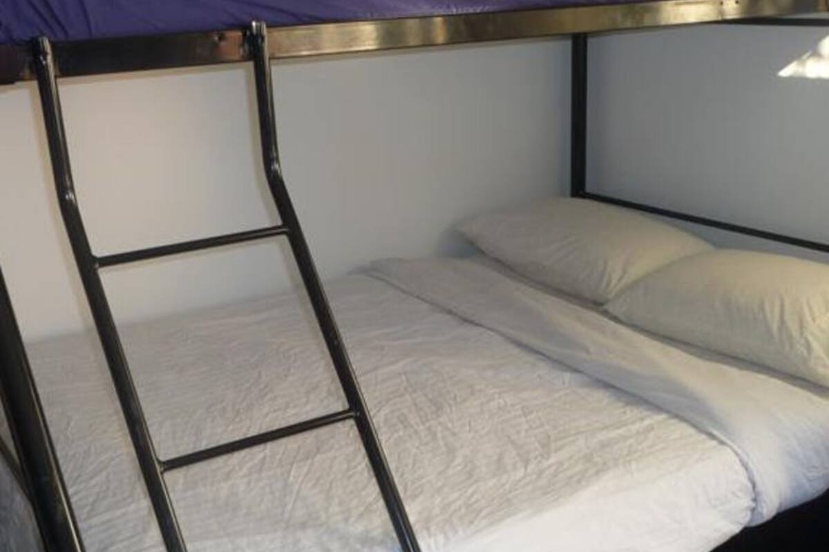 Una cama individual con escalera, ropa de cama blanca y estructura metálica.