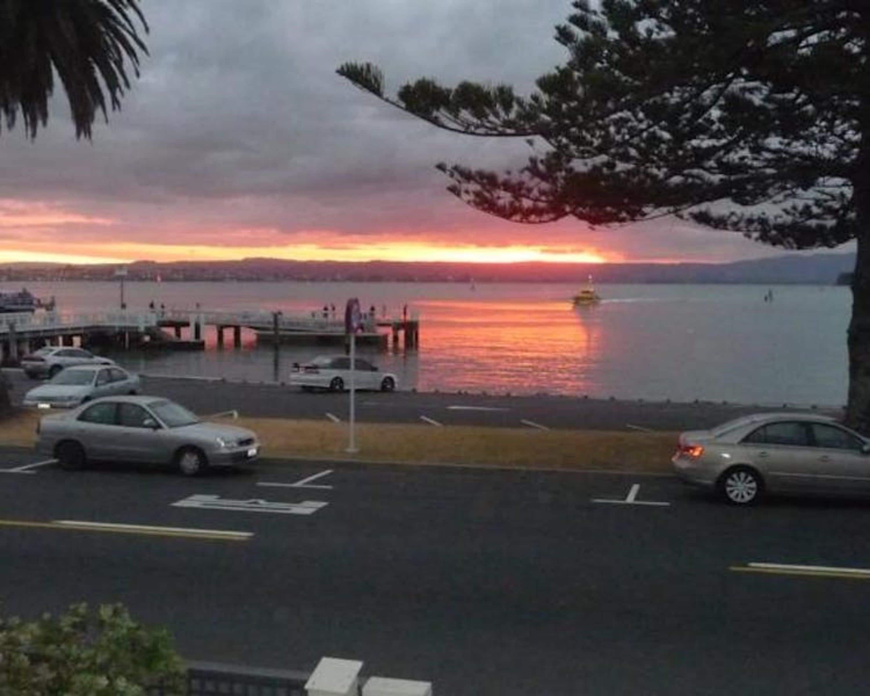 A parking area with cars and a waterfront view during sunset.