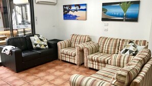 Un salon avec un canapé en cuir noir, deux fauteuils à rayures et un sol carrelé.