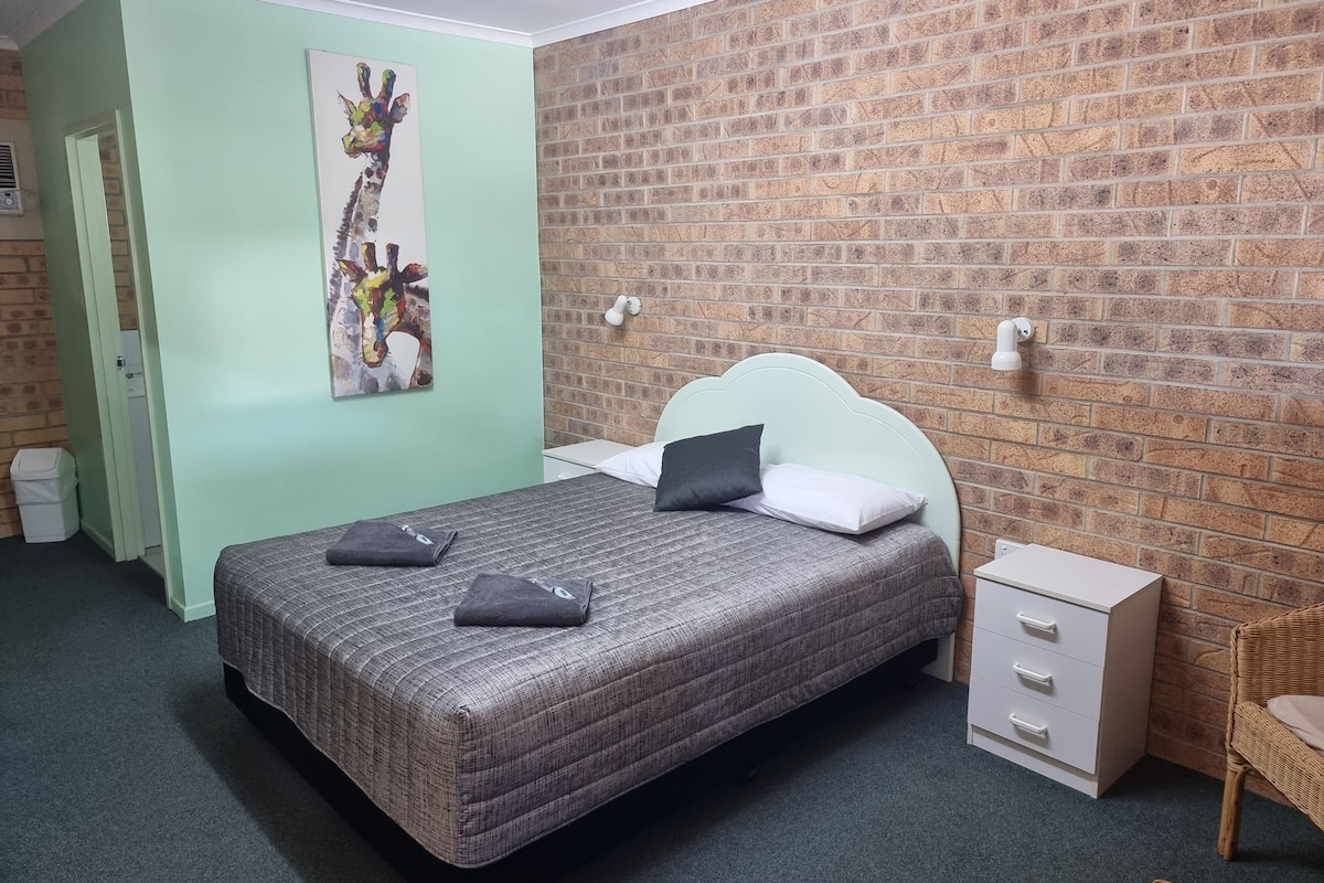 Un dormitorio con una cama, una mesita de noche, una silla y una pared con diseño de ladrillo.