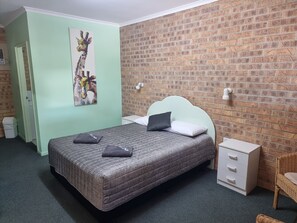 A bedroom with a bed, a nightstand, a chair, and a brick-patterned wall.