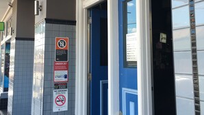 La entrada del Hotel Strathfield, con una puerta azul, un letrero que indica prohibido fumar y un aviso de no acceso para menores de 25 años.