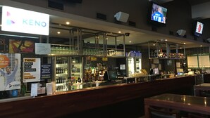 Zona de bar con un letrero de KENO, múltiples pantallas y una variedad de botellas y vasos en estanterías.