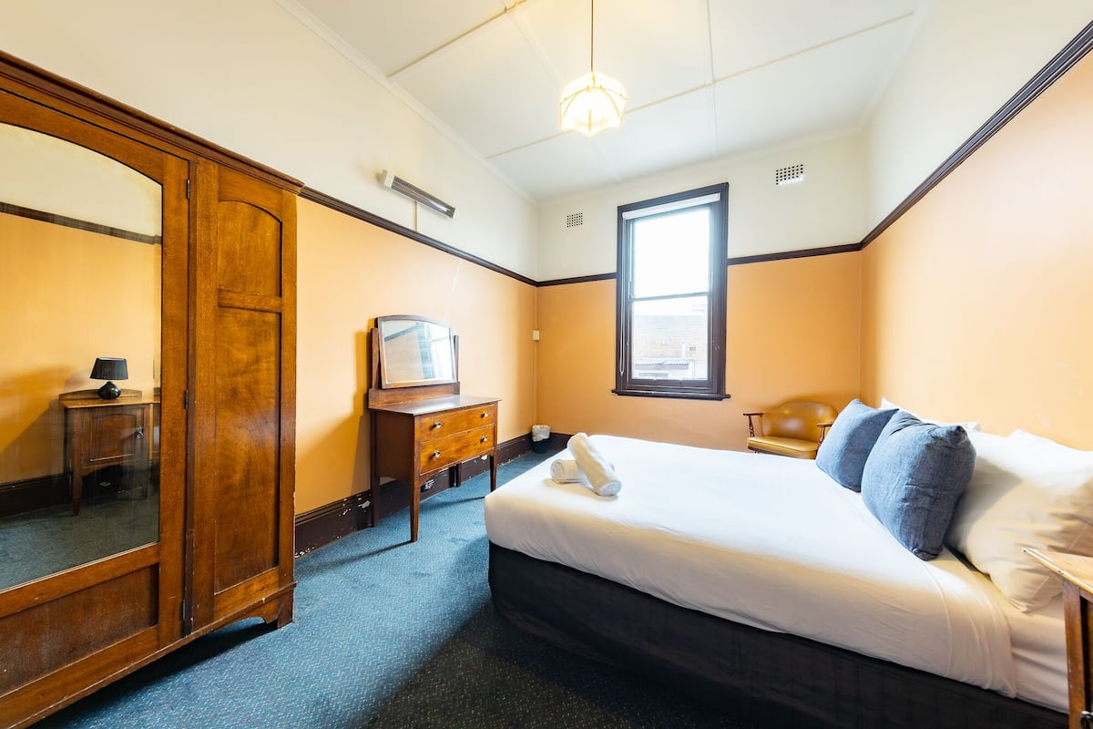 A hotel room with a bed, a dresser, a mirror, a window, and a ceiling light.
