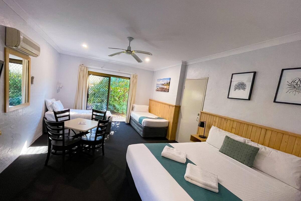 A hotel room with a bed, a desk, a chair, a ceiling fan, and a window with curtains.